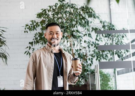 felice uomo d'affari asiatico con tatuaggio che tiene il caffè per andare a guardare la macchina fotografica, la vita aziendale Foto Stock