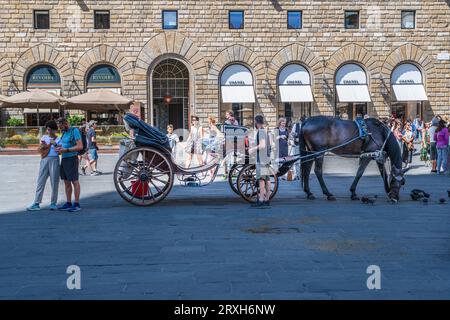 Firenze, Italia - 1 settembre 2023. Una foto di un cavallo, di una carrozza e di un autista che riposa nella splendida Piazza della Signoria mentre i turisti passano a Floren Foto Stock