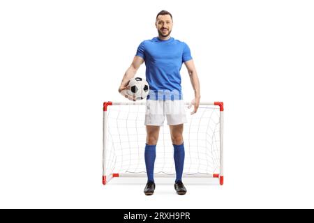 Ritratto completo di un giocatore di calcio che tiene una palla davanti a un mini goal isolato su sfondo bianco Foto Stock