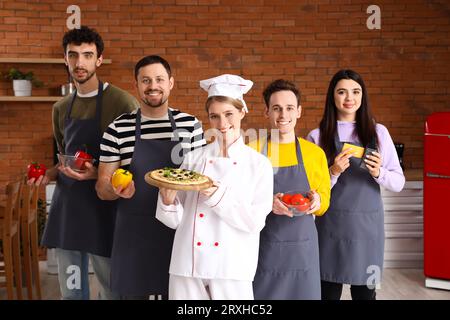 Chef donna con pizza italiana preparata e gruppo di giovani dopo la lezione di cucina in cucina Foto Stock