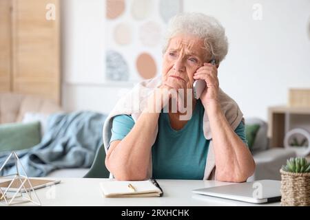 Donna anziana triste che parla al telefono cellulare a casa Foto Stock