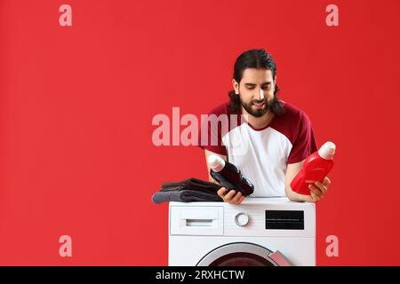 Giovane con detergenti vicino alla lavatrice su sfondo rosso Foto Stock