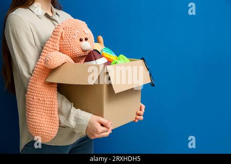 Donna che tiene una scatola di oggetti indesiderati per la vendita in giardino su sfondo blu Foto Stock