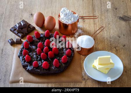 Torta di cioccolato e lamponi con ingredienti su un tavolo di legno Foto Stock