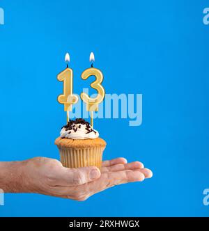 Dolce di compleanno consegnato a mano - candela numero 13 su sfondo blu Foto Stock