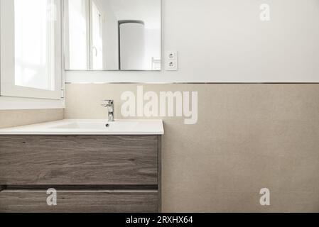 Parete del bagno con un armadio in legno nuovo di zecca con lavandino in porcellana bianca e specchio quadrato senza cornice appeso alla parete Foto Stock