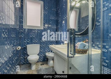 bagno con armadio in legno con lavabo in porcellana bianca, cabina doccia e piastrelle blu vintage alle pareti Foto Stock