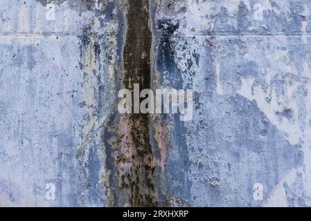 Una parete con vernice sbucciante e macchie di umidità dovute all'acqua che scorre lungo la superficie Foto Stock