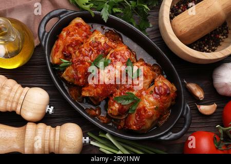 Deliziosi involtini di cavolo ripieni cucinati con salsa di pomodoro e ingredienti su un tavolo di legno, piatti Foto Stock