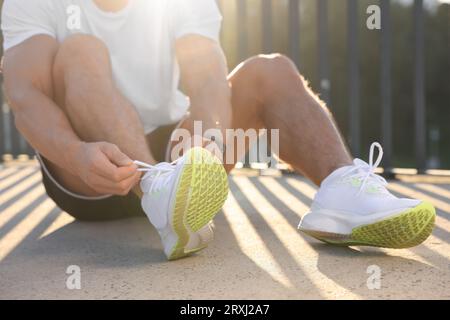 Uomo che stringe le scarpe prima di correre all'aperto nelle giornate di sole, primo piano Foto Stock