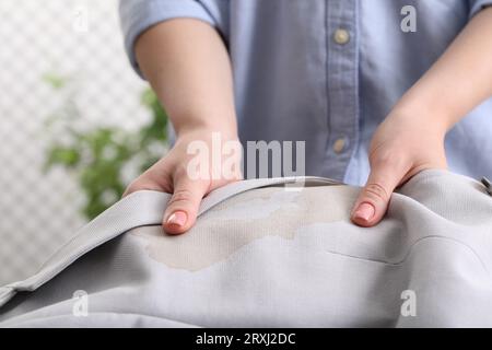 Donna che mostra macchie di caffè sulla giacca su sfondo sfocato, primo piano Foto Stock