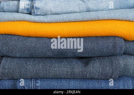 Una pila di vestiti piegata in modo ordinato: Jeans in diverse tonalità di blu e un maglione giallo brillante in mezzo. Foto Stock
