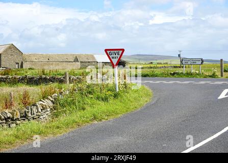 Incrocio di crocevia rurale su Orkney Island, Scozia. Un cartello triangolare consiglia ai conducenti di "cedere" o di "cedere" al traffico sull'autostrada principale Foto Stock