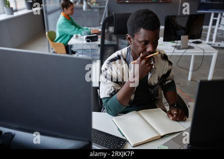 Programmatore professionale penoso che sviluppa nuovi progetti mentre è seduto sul posto di lavoro Foto Stock