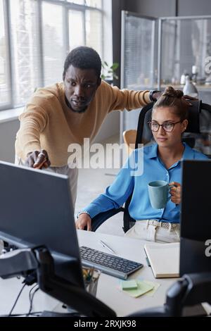 Immagine verticale di giovani colleghi che discutono di una presentazione al computer in team durante il lavoro in ufficio IT Foto Stock