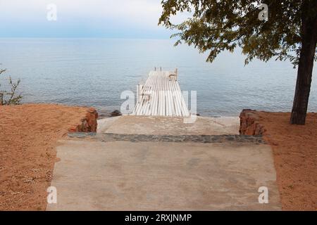 Molo in legno con panchine con strada alberata e in pietra sulla spiaggia al mare. Riposo, viaggio, tranquillità, tramonto e alba. Copia spazio Foto Stock