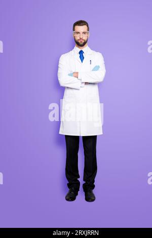 Ritratto integrale di elegante e bello scienziato con stoppia in abito bianco con cravatta blu con le braccia incrociate guardando la fotocamera Foto Stock