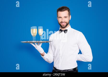 Ritratto di allegro amico uomo in classica camicia bianca e arco nero tenendo la mano dietro la schiena e vassoio con tre bicchieri di champaign Foto Stock