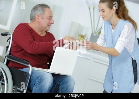 accompagnatore che dà un drink a un uomo in sedia a rotelle Foto Stock