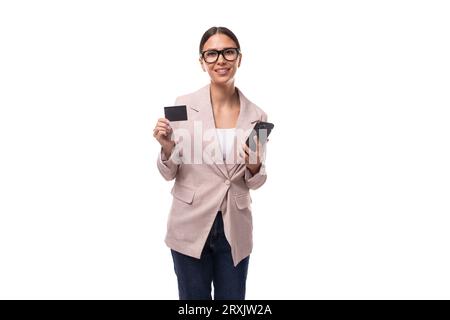 giovane donna caucasica con i capelli neri raccolti in una coda di cavallo vestita con una giacca beige contiene un mockup di plastica per la pubblicità bancaria Foto Stock