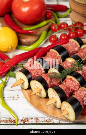 Kebab di melanzane su fondo di legno. Kebab crudo di melanzane shish con erbe e spezie Foto Stock