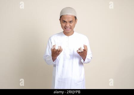 Ritratto di un attraente uomo musulmano asiatico in camicia bianca che fa gesto della mano arrabbiato con le dita. Immagine isolata su sfondo grigio Foto Stock