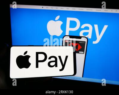 Persona che possiede uno smartphone con il logo del servizio di pagamento mobile Apple Pay sullo schermo di fronte al sito Web. Concentrarsi sul display del telefono. Foto Stock