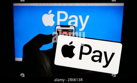 Persona che possiede un cellulare con il logo del servizio di pagamento mobile Apple Pay sullo schermo davanti alla pagina Web aziendale. Concentrarsi sul display del telefono. Foto Stock