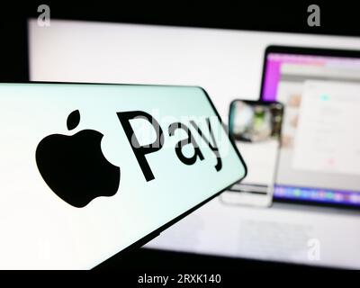 Cellulare con logo del servizio di pagamento mobile Apple Pay sullo schermo di fronte al sito Web dell'azienda. Mettere a fuoco il display centrale sinistro del telefono. Foto Stock