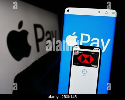 Persona che possiede uno smartphone con sito Web del servizio di pagamento mobile Apple Pay sullo schermo davanti al logo. Concentrarsi sul centro del display del telefono. Foto Stock