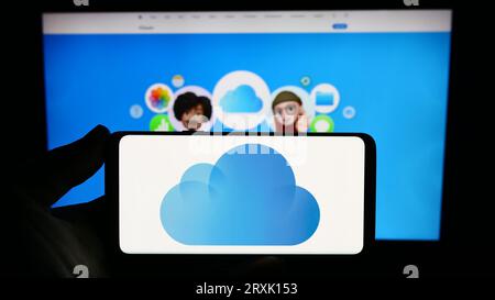 Persona che possiede uno smartphone con il logo della piattaforma di archiviazione cloud Apple iCloud sullo schermo davanti al sito Web. Concentrarsi sul display del telefono. Foto Stock