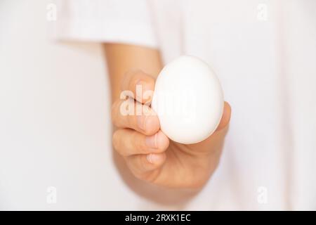 La mano di una donna tiene un uovo bianco su sfondo bianco da vicino Foto Stock