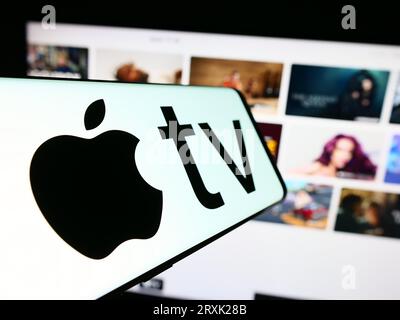 Smartphone con logo del servizio di streaming video Apple TV Plus sullo schermo di fronte al sito Web aziendale. Mettere a fuoco il display centrale sinistro del telefono. Foto Stock