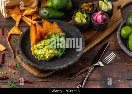 Guacamole all'avocado con tortillas croccanti su un piatto di pietra nera su un tavolo di legno Foto Stock