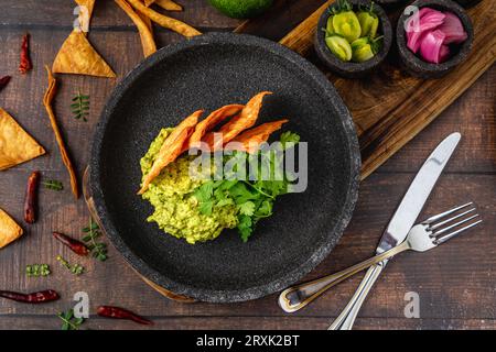Guacamole all'avocado con tortillas croccanti su un piatto di pietra nera su un tavolo di legno Foto Stock