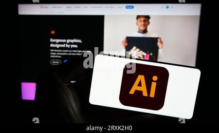 Persona che possiede uno smartphone con il logo dell'editor di grafica vettoriale Adobe Illustrator sullo schermo davanti al sito Web. Concentrarsi sul display del telefono. Foto Stock