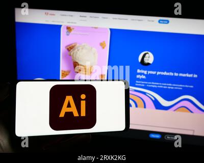Persona che possiede il cellulare con il logo dell'editor di grafica vettoriale Adobe Illustrator sullo schermo davanti alla pagina Web aziendale. Concentrarsi sul display del telefono. Foto Stock