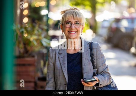 Ritratto di una donna anziana sorridente con il cellulare in strada Foto Stock