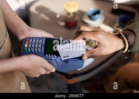 Primo piano di un uomo afroamericano che paga il pranzo con carta di credito mentre è seduto al bar Foto Stock