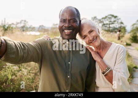 Ritratto selfie di una coppia anziana multietnica che sorride davanti alla fotocamera durante la passeggiata all'aperto Foto Stock