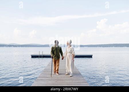 Coppia di anziani multietnici che si tiene per mano mentre cammina lungo il molo Foto Stock