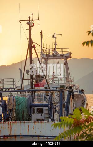 Un vecchio peschereccio arrugginito e stagionato è ancorato nella baia tra le montagne, al tramonto. Foto Stock