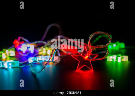 Primo piano delle colorate luci elettriche di natale garland a forma di stelle, moderno arredamento per le vacanze su nero Foto Stock