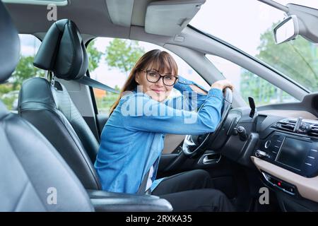 Autista di mezza età seduto al volante in auto, sorridente guardando la fotocamera Foto Stock