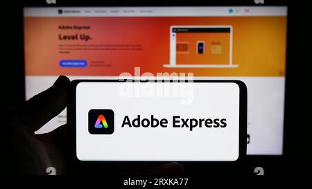 Persona che possiede lo smartphone con il logo del software di grafica Adobe Express sullo schermo davanti al sito Web. Concentrarsi sul display del telefono. Foto Stock