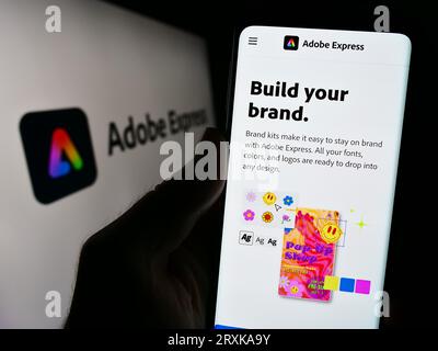 Persona che tiene il cellulare con una pagina Web del software di grafica Adobe Express sullo schermo davanti al logo. Concentrarsi sul centro del display del telefono. Foto Stock