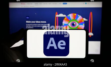 Persona che possiede lo smartphone con il logo del software di grafica animata Adobe After Effects sullo schermo davanti al sito Web. Concentrarsi sul display del telefono. Foto Stock