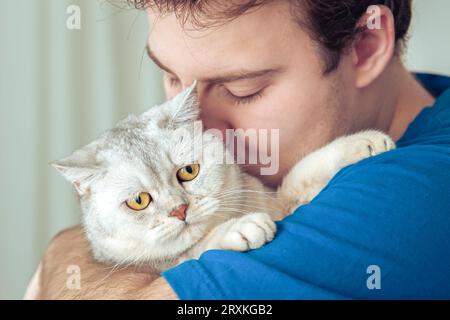 Primo piano del volto di un uomo che tiene in mano il suo grazioso gatto inglese. Foto Stock