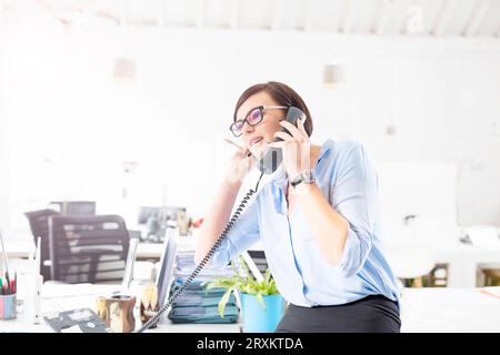 Imprenditrice con gli occhiali parlando al telefono in ufficio Foto Stock