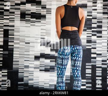 Donna in abbigliamento sportivo in piedi contro un muro a mosaico Foto Stock